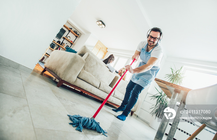 Husband housekeeping and cleaning concept. A man cleans the house, while women gossiping on the sofa