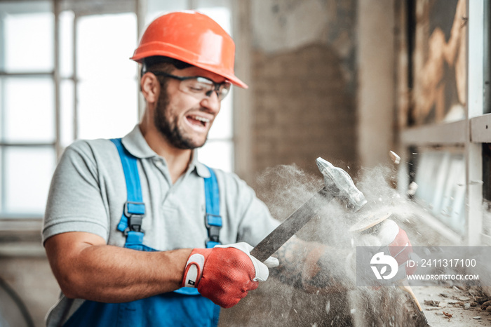 Builder, working, destroys a wall with his hammer, screaming and smiling