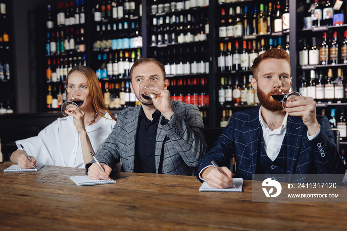 Friends tasting red wine sommeliers and taking notes at degustation notepad