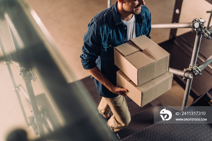 cropped view of positive businessman holding boxes and walking on stairs in new office