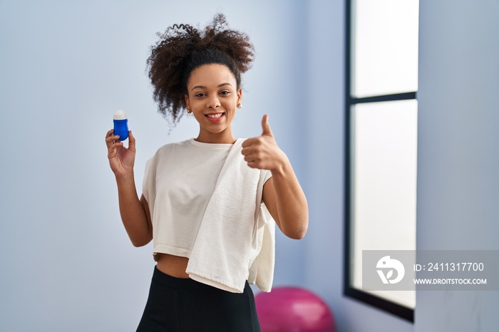 Young african american woman wearing sportswear and towel holding deodorant smiling happy and positive, thumb up doing excellent and approval sign