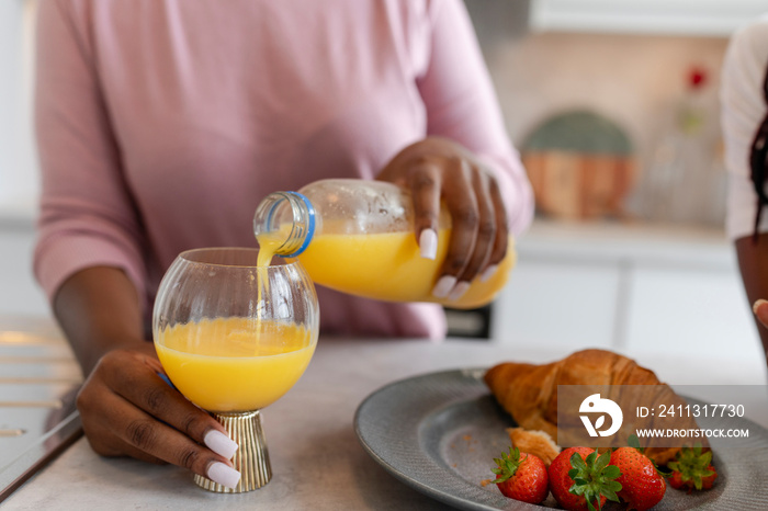 Woman pouring orange juice into glass for breakfast at home