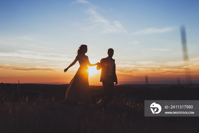 Silhouette of loving couple in rays of sun. Newlyweds walking outdoor