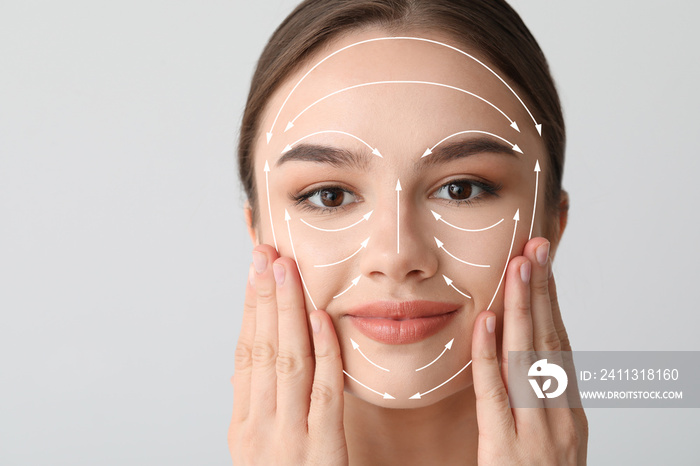 Beautiful woman massaging her face against light background