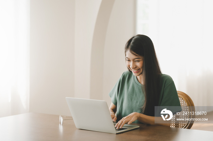 Smiling asian young woman working on laptop at home office. Young asian student using computer remote studying, virtual training, e-learning, watching online education webinar at house