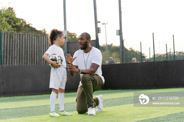 Man instructing girl (6-7) with ball on soccer field