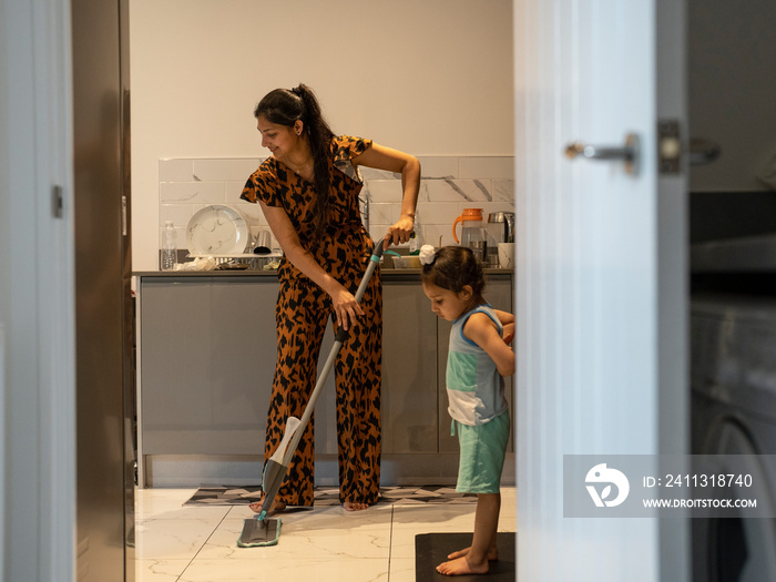 Young woman mopping floor while son (2-3) watching