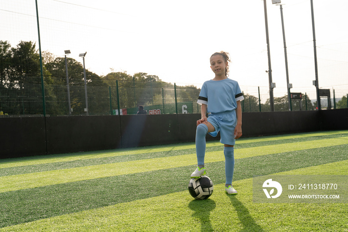 Portrait of girl (6-7) with ball on soccer field