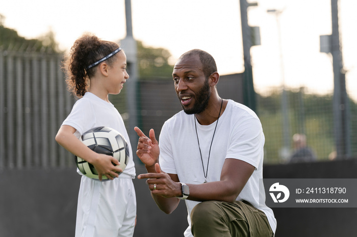 Man instructing girl (6-7) with ball on soccer field