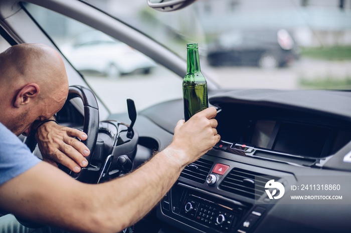 Drunk adult man drives a car with a bottle of beer. Driver under alcohol influence.