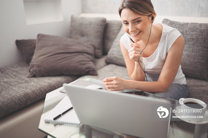 Attractive happy young student studying online at home, using laptop computer, headphones, having video chat, waving. Remote work, distance education. Video conference or virtual event on quarantine