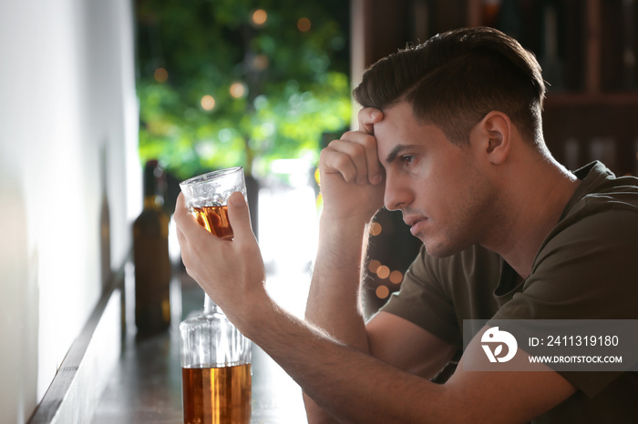 Young man with glass of drink in bar. Alcoholism problem