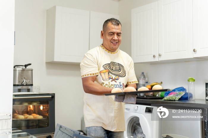 Man holding tray of freshly baked buns in kitchen