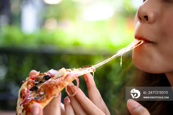 Pizza look so yummy or delicious food. Charming beautiful asia woman is eating pepperoni pizza and sticky mozzarella cheese. Attractive girl feels hungry and loves the taste. She sit at restaurant