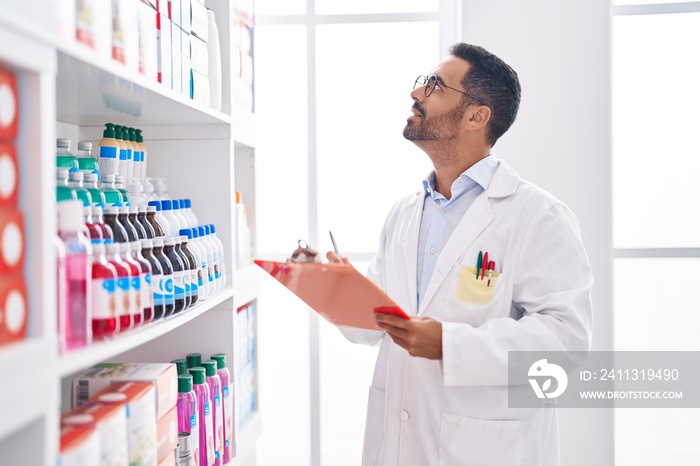 Young hispanic man pharmacist smiling confident writing on document at pharmacy