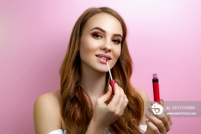 Girl puts lipstick on a pink background