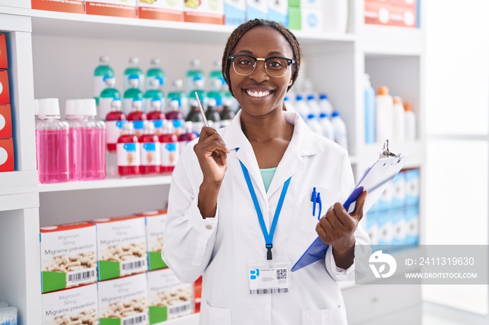 African american woman pharmacist smiling confident holding clipboard at pharmacy