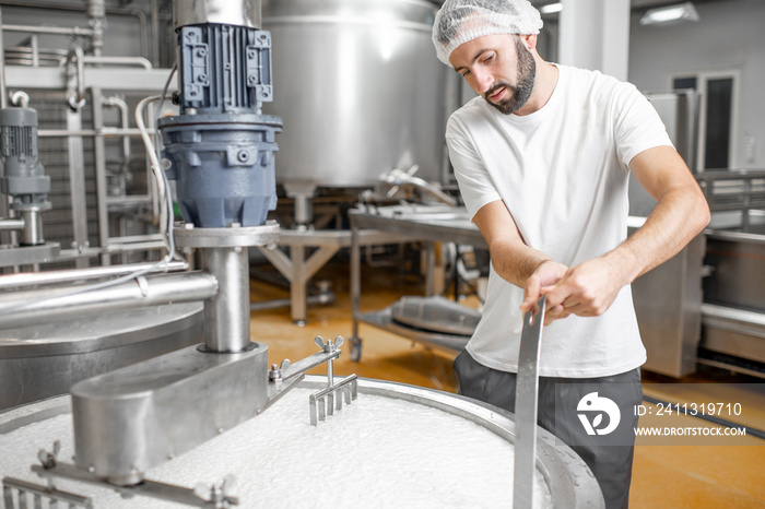 Man mixing milk in the stainless tank during the fermentation process at the cheese manufacturing