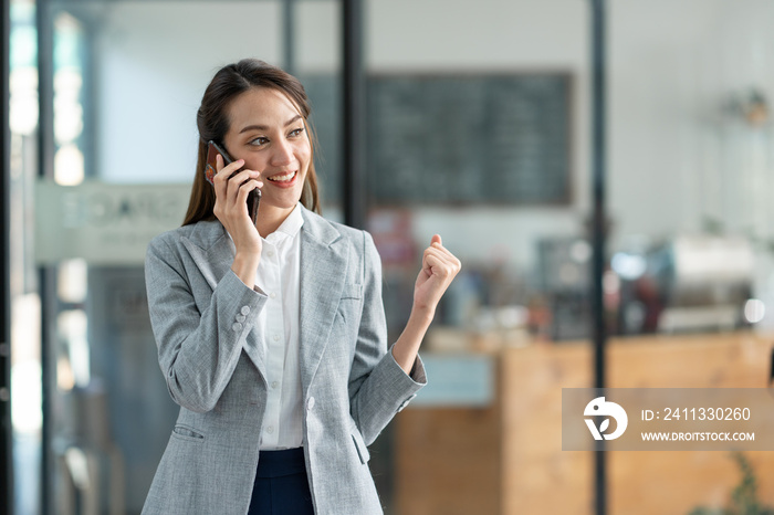 Attractive Asian businesswoman standing on the phone talking about real estate projects and chatting with happy smiles at the office.