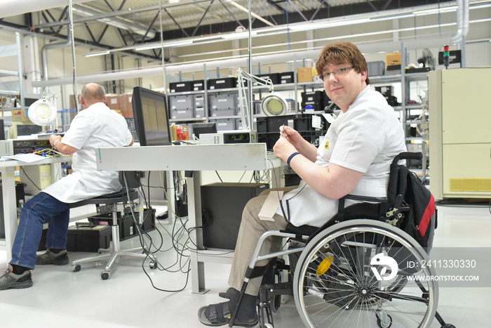 handicapped worker in a wheelchair at a workplace in a electronics manufacturing and assembly factory