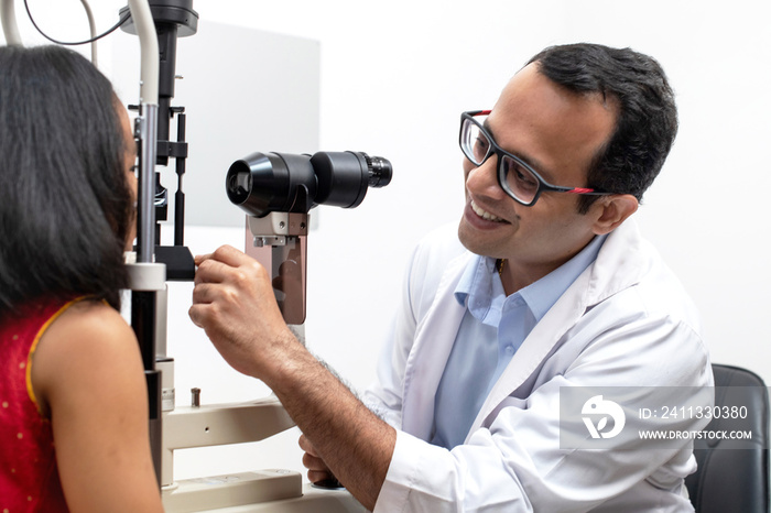 Indian girl and optometrist doing eye test with slit lamp in modern ophthalmology clinic, checking retina of a girl eye