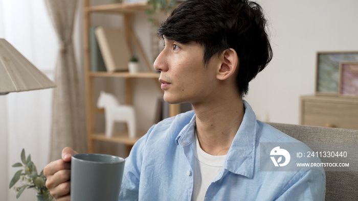 cheerful asian japanese young male looking out of window and enjoying the tranquil morning and coffee from cup in the living room at home