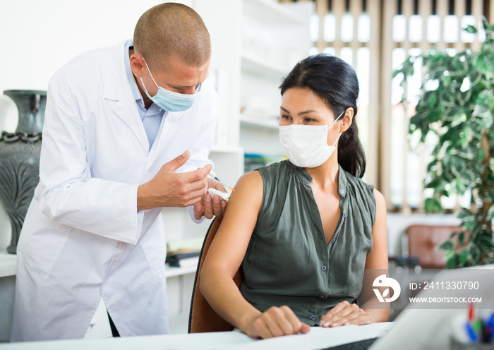 Doctor in a protective face mask giving coronavirus vaccine to pacient in modern office