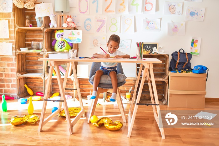 Beautiful african american toddler sitting drawing using paper and pencils on desk at kindergarten