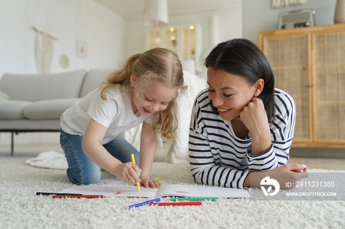 Mom, adopted child daughter draw with colorful pencils, lying on floor. Happy motherhood, adoption