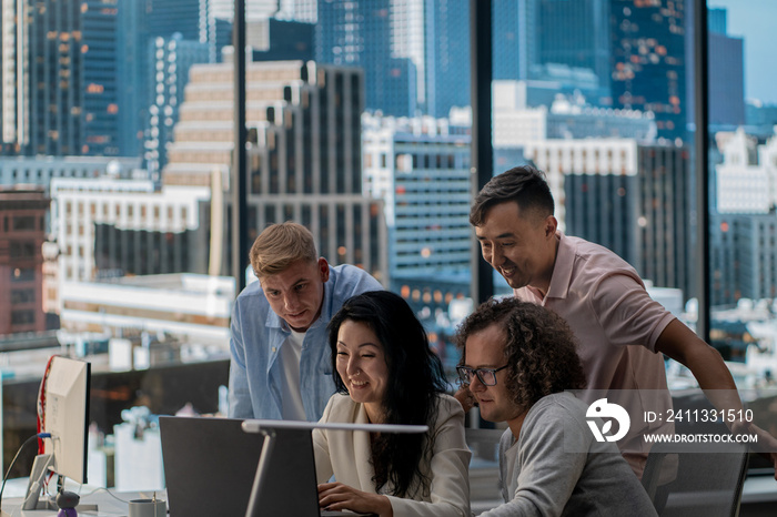 Diverse team of employees brainstorming, gathering around the computer screen. Discussing project, new ideas, company development