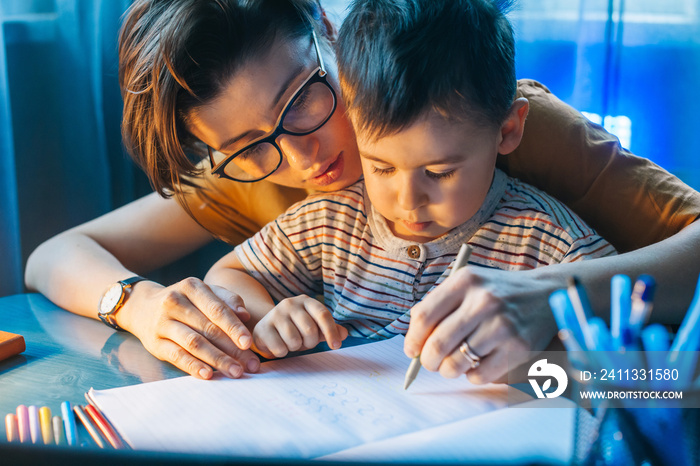 Little boy doing homework at home with school books helped by his mother. For lifestyle design. Family care. Children education. Family day.