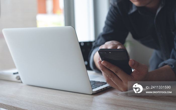 Man using mobile phone during online working on laptop computer at home office