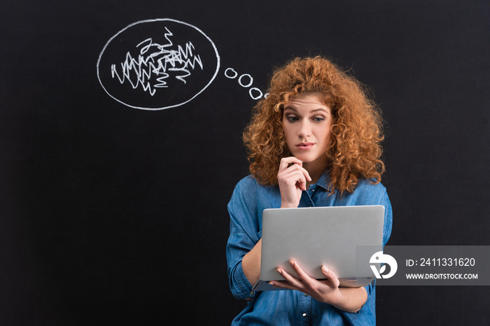 skeptical redhead girl using laptop with thought bubble on blackboard