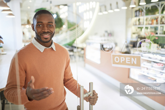 Waist up portrait of smiling Adrian-American man opening cafe in morning and welcoming guests, copy space