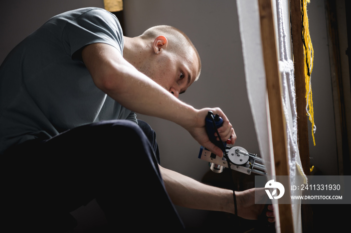 Young artisan with tufting machine making rug on canvas