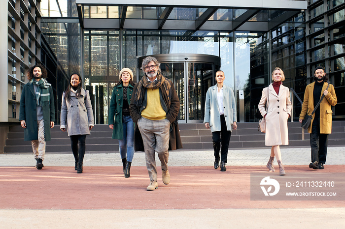 A multi-ethnic group of cheerful business people walking towards the camera outside a corporate center. High quality photo