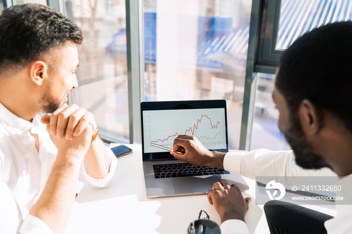 .Two multiracial businessmen on laptop looking at company growth chart