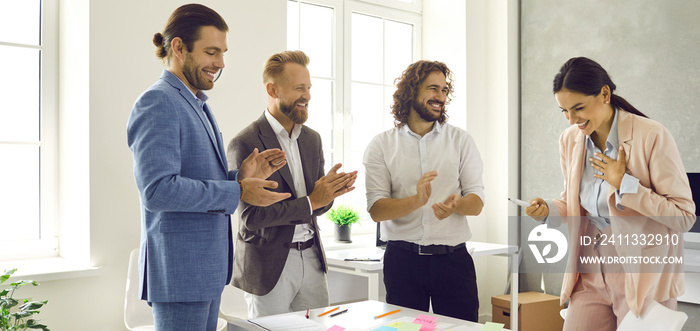 Cheerful business people applaud their female colleague at a meeting in the office. Male colleagues applaud to support her presentation. Happy woman bows thanking the participants of a meeting.