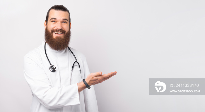 Portrait of bearded doctor man, medical professional holding something in empty hand isolated over white background