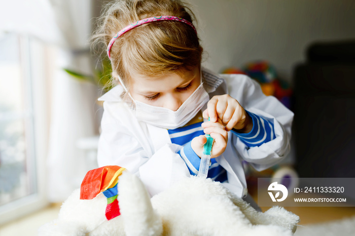 Little Little girl makes injection to teddy bear. Cute child with medical mask playing doctor, holding syringe with vaccine. Coronavirus covid vaccination concept.