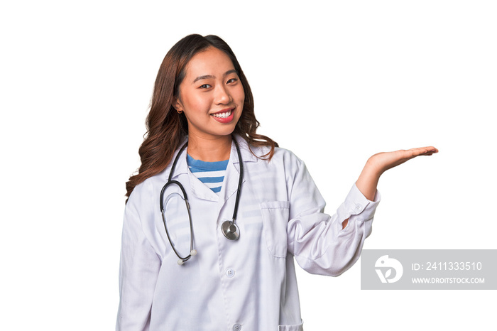 A young asian doctor woman showing a copy space on a palm and holding another hand on waist.