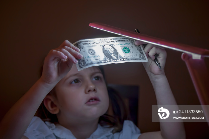 Portrait of cute little business child girl checking US Dollar banknote for watermark.