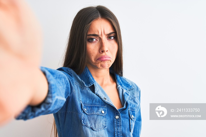 Beautiful woman wearing denim shirt make selfie by camera over isolated white background depressed and worry for distress, crying angry and afraid. Sad expression.