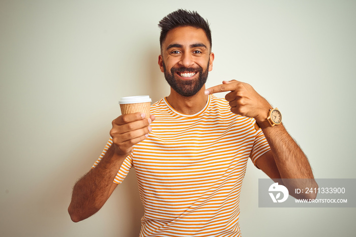 Young indian man drinking cup of coffee standing over isolated white background very happy pointing with hand and finger