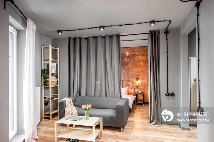 Modern living room in loft style made in grey colors with sofa and bedroom behind the curtains