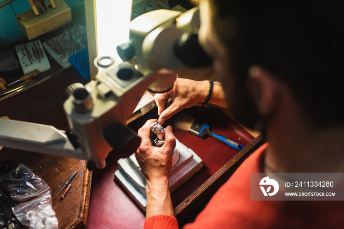 Unrecognizable jeweler hands working on a piece of jewelry at his workbench inside his workshop.