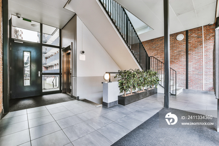 Staircase and elevator located near door and brick wall in hall of contemporary apartment building