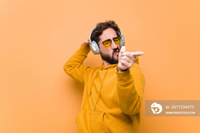 young crazy cool man listening music with headphones against orange wall