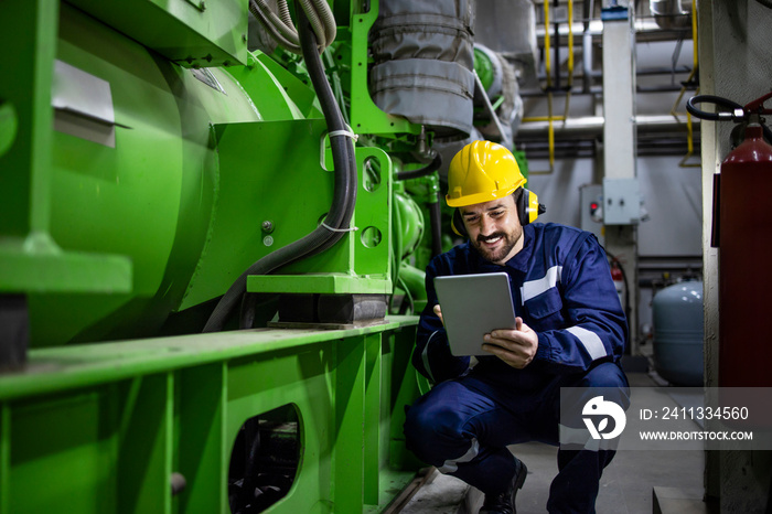 Caucasian worker or serviceman checking diagnostics of large industrial generator in power plant.