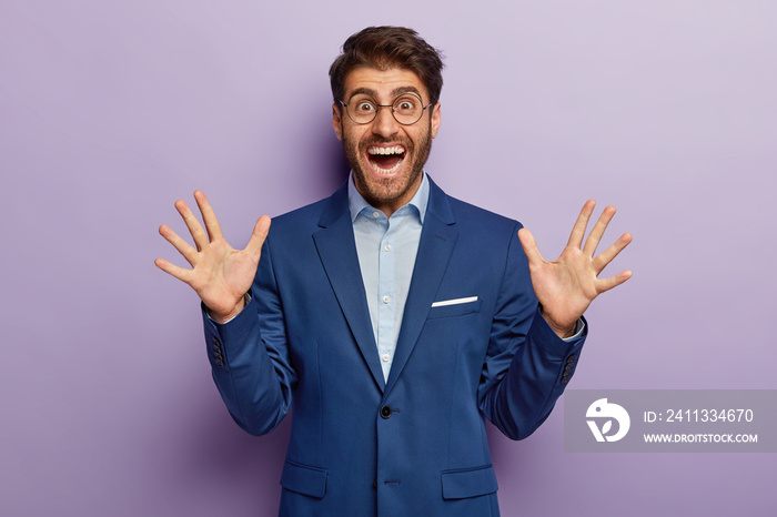 Cheerful male banker in elegant outfit, smiles and shows palms, happy to meet with former colleague, isolated on purple background. Successful entrepreneur rejoices new investments in his business